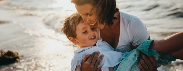Parent holding a smiling child wrapped in a towel at the beach