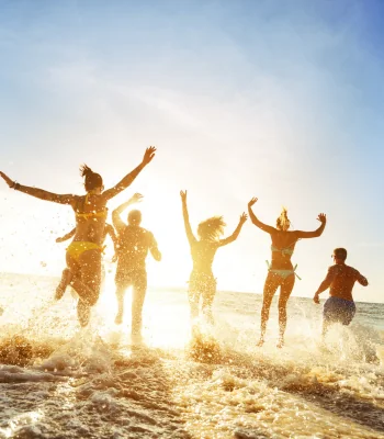 Group of friends laughing and running into the ocean at the beach