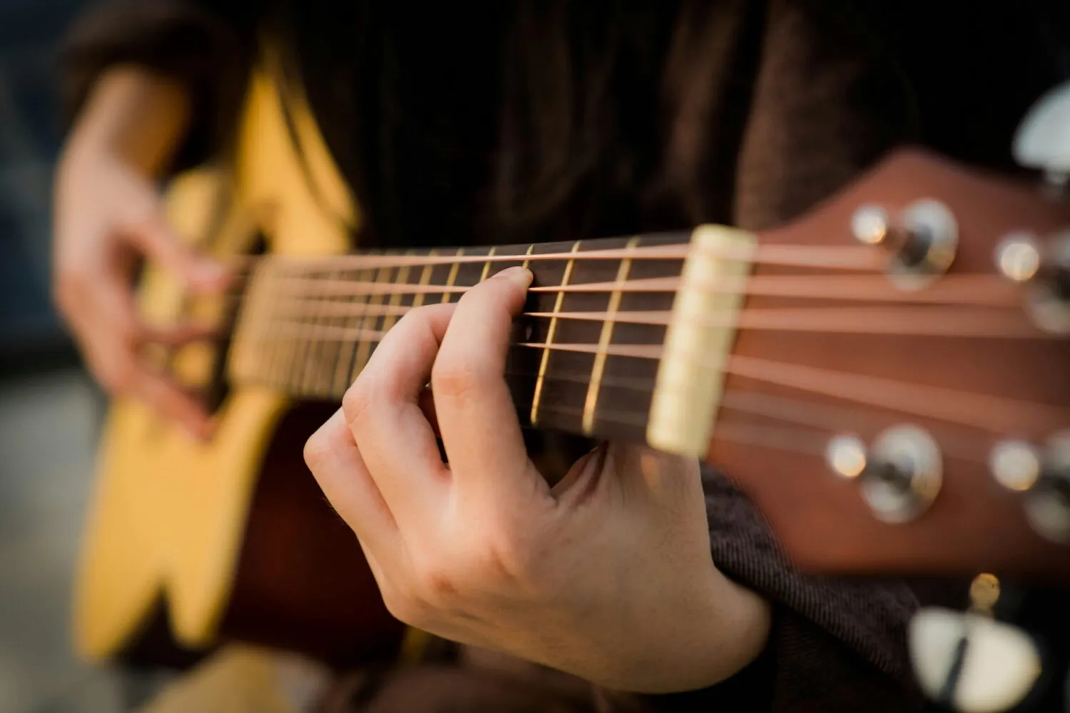 Man playing acoustic guitar outdoors in a relaxed, social setting