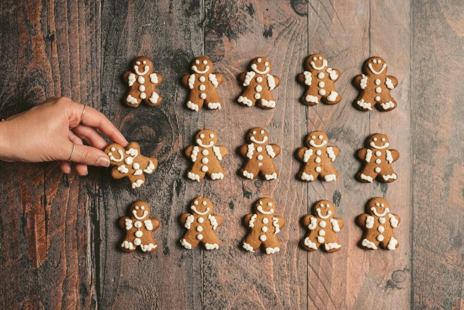 Hand placing gingerbread cookies in neat rows on a wooden table
