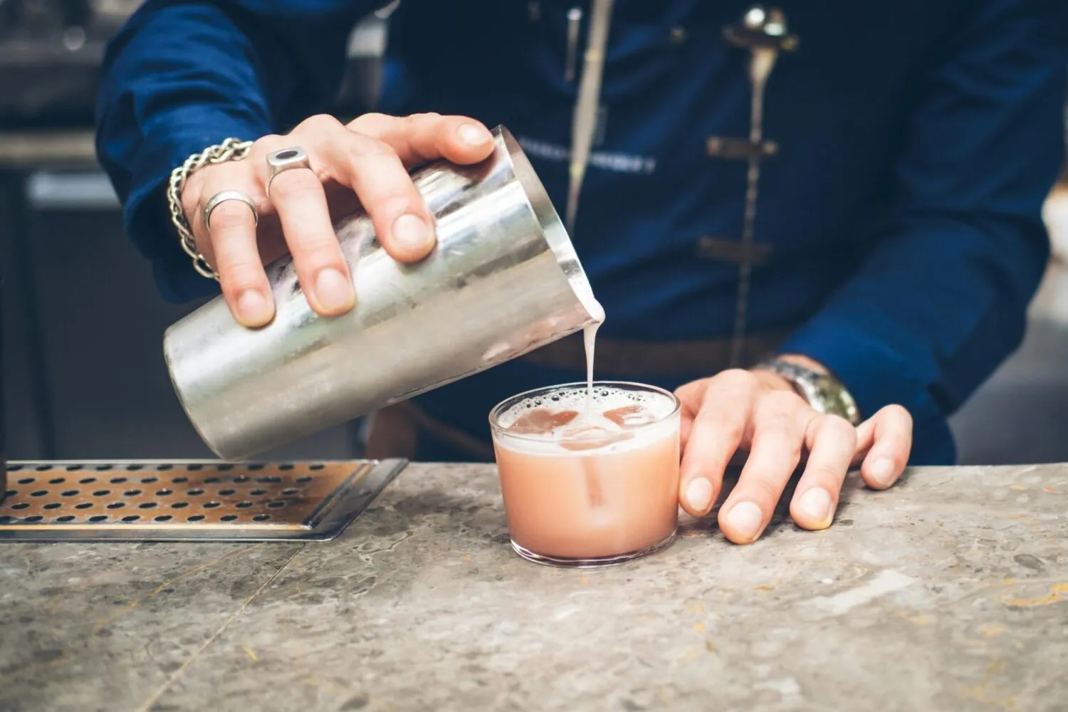 Bartender pouring foam onto a pink cocktail at a bar counter