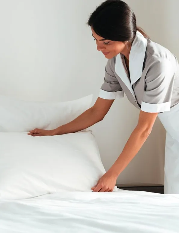 Housekeeper smoothing fresh white bedding on a neatly made bed