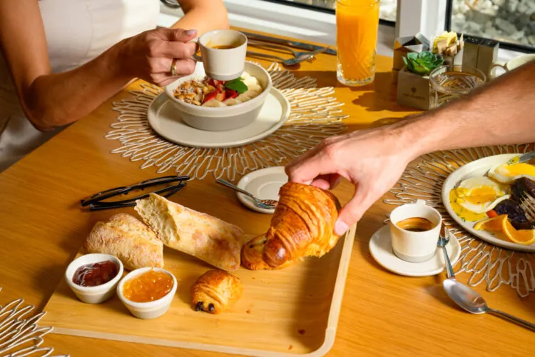 Guest reaching for a croissant from a breakfast tray on a wooden table