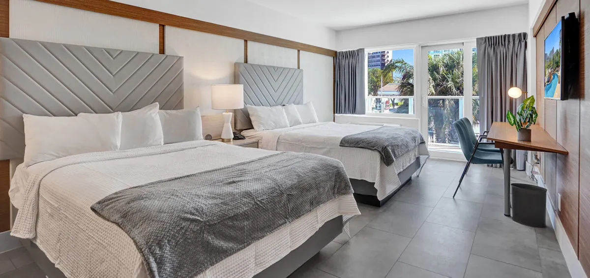 Two queen beds with upholstered headboards, balcony doors, and seating area