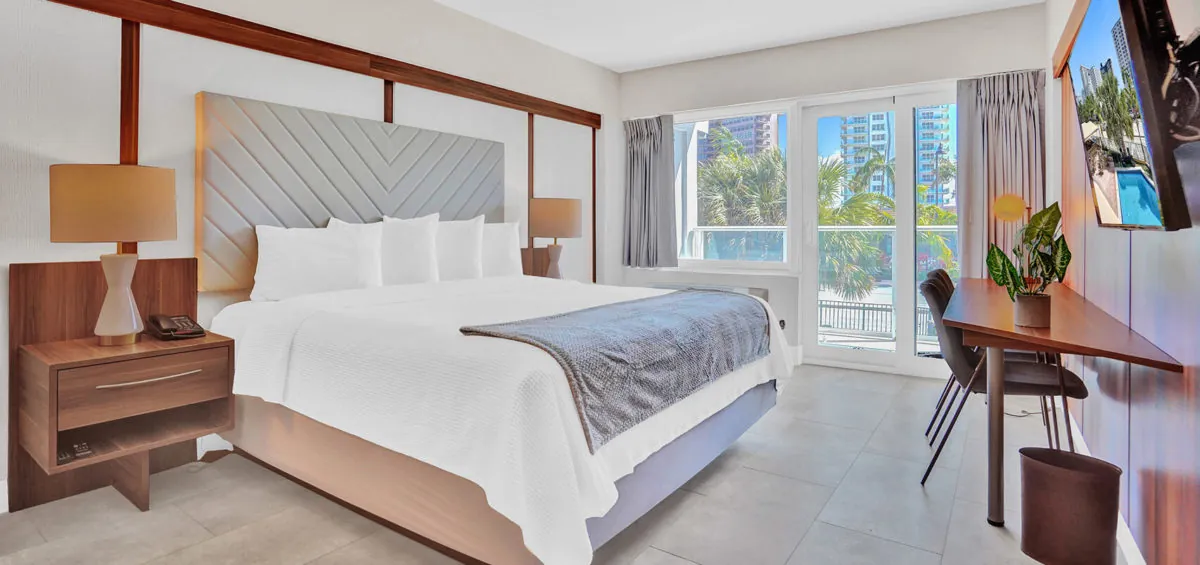 King bed with upholstered headboard, balcony access, and writing desk