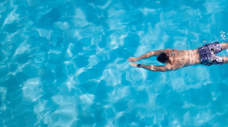 Person swimming freestyle across a clear blue outdoor pool