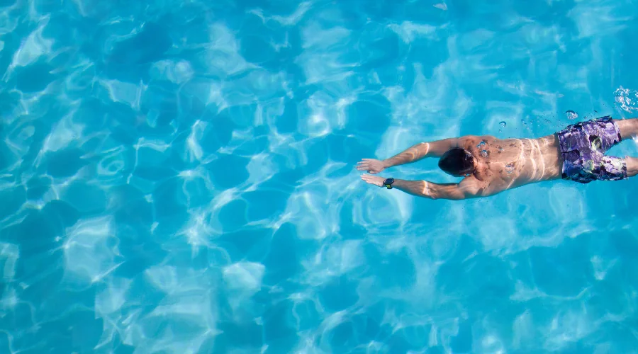Person swimming freestyle across a clear blue outdoor pool