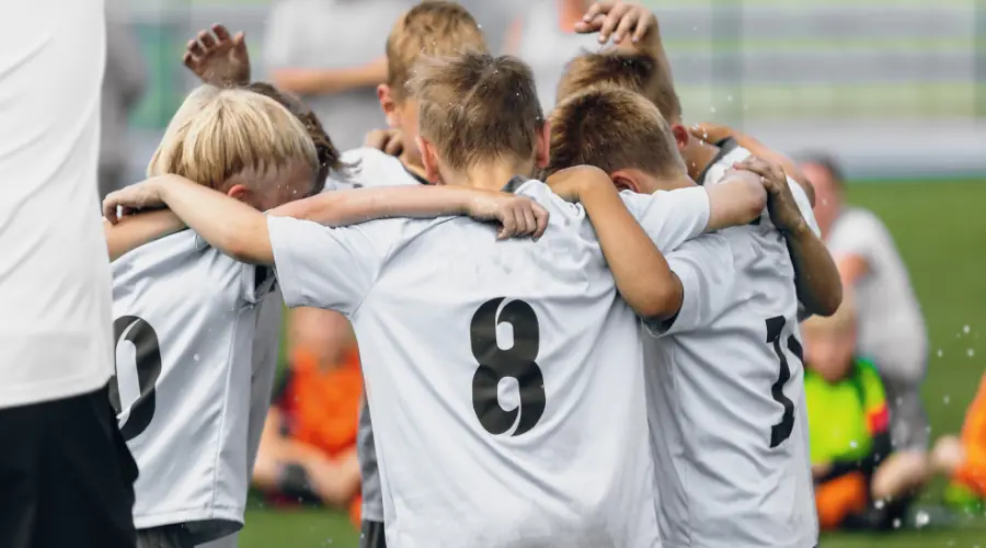 Youth football team celebrating with arms around each other on a field