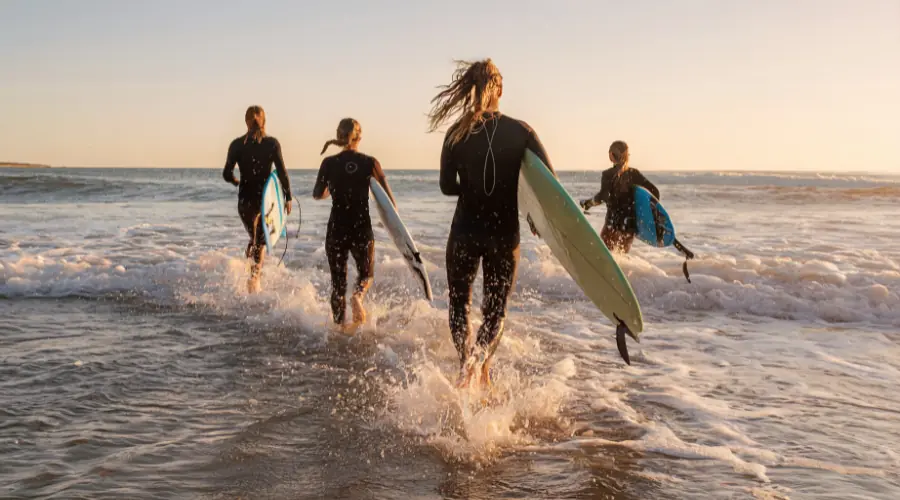 Group of surfers walking into the ocean carrying surfboards at sunset