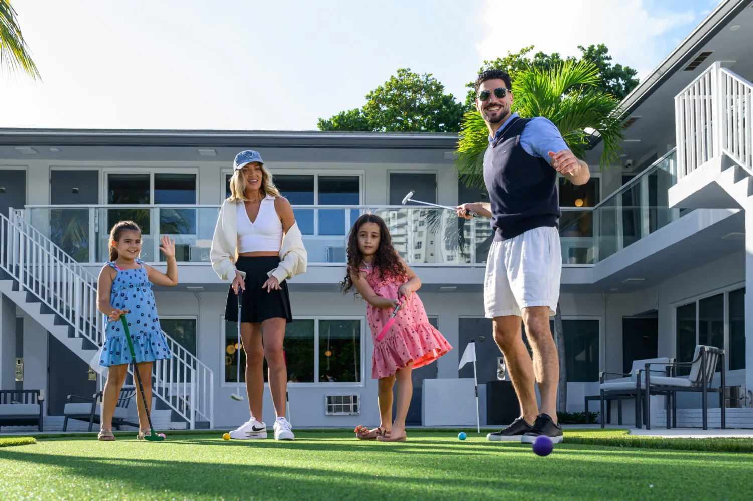 Family playing lawn games on a grassy courtyard between hotel buildings