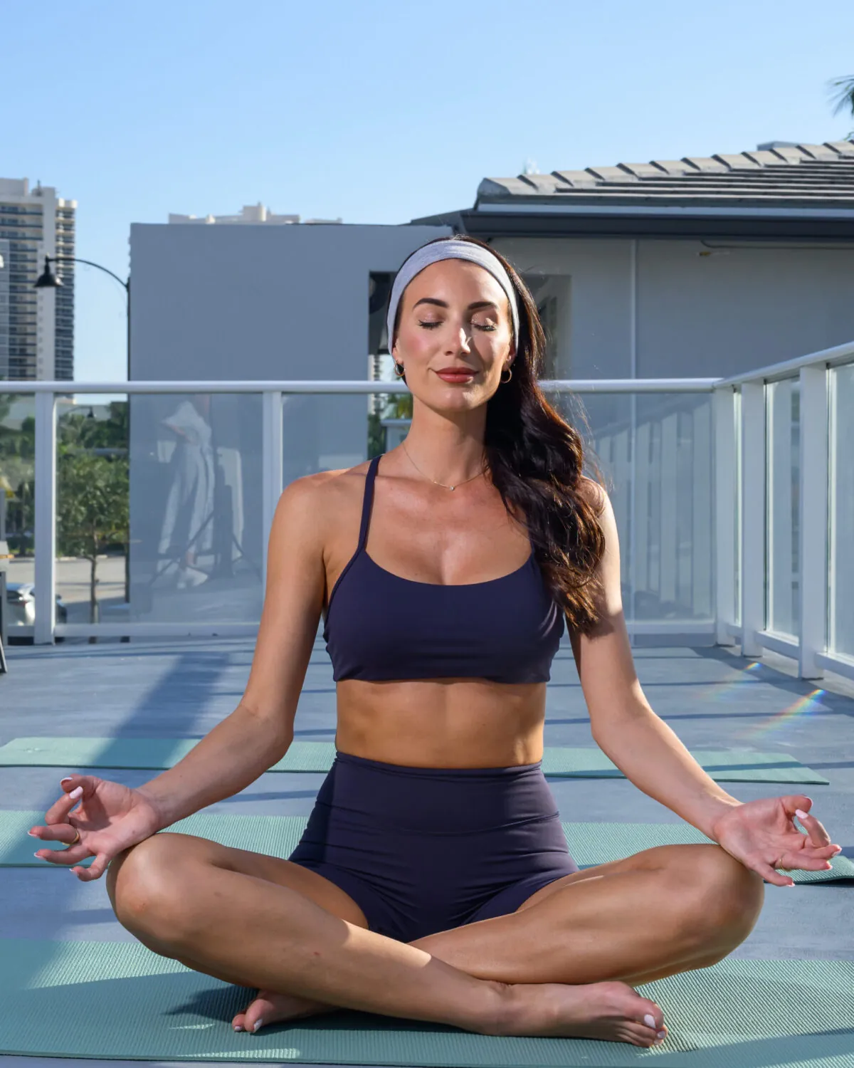 Woman sitting cross-legged on a rooftop deck, meditating in activewear