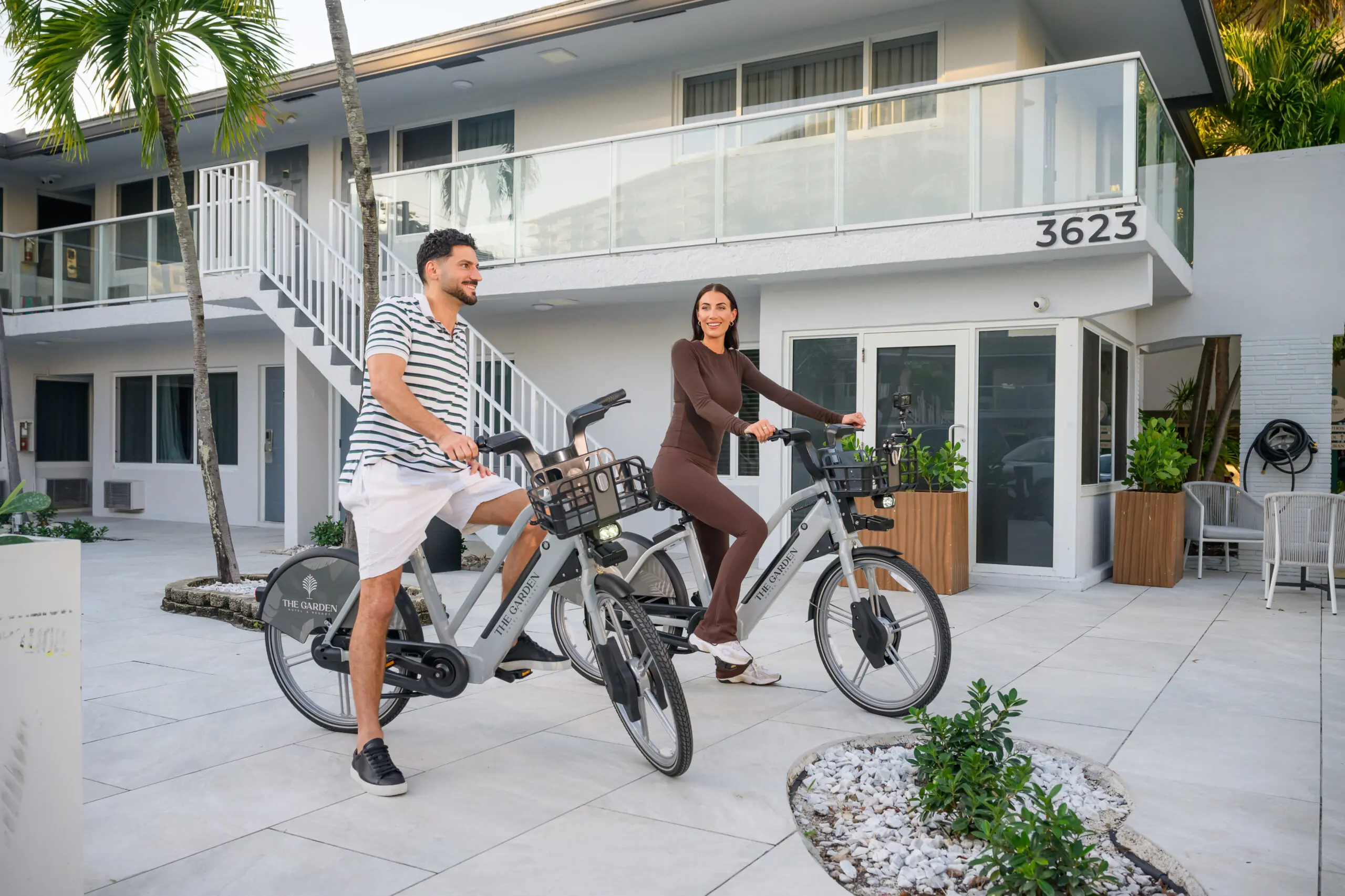 Two guests riding bicycles through a landscaped hotel courtyard
