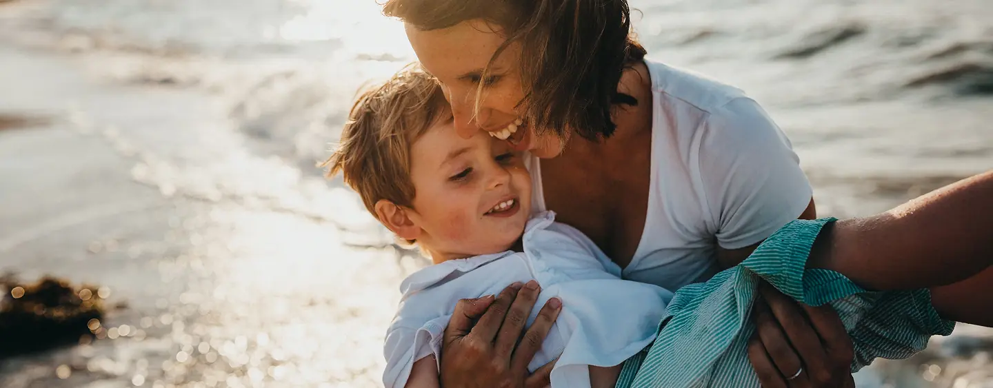 Parent holding a smiling child wrapped in a towel at the beach